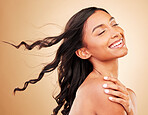 Curly hair, smile and woman in wind at studio isolated on a brown background. Hairstyle breeze, natural cosmetics and happy Indian model in salon treatment for beauty care, hairdresser and balayage