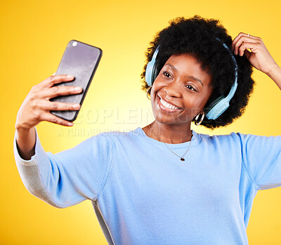 Buy stock photo Happy black woman, phone and selfie with headphones for listening to music against a yellow studio background. African female person smile, afro or mobile smartphone app in photography or podcast