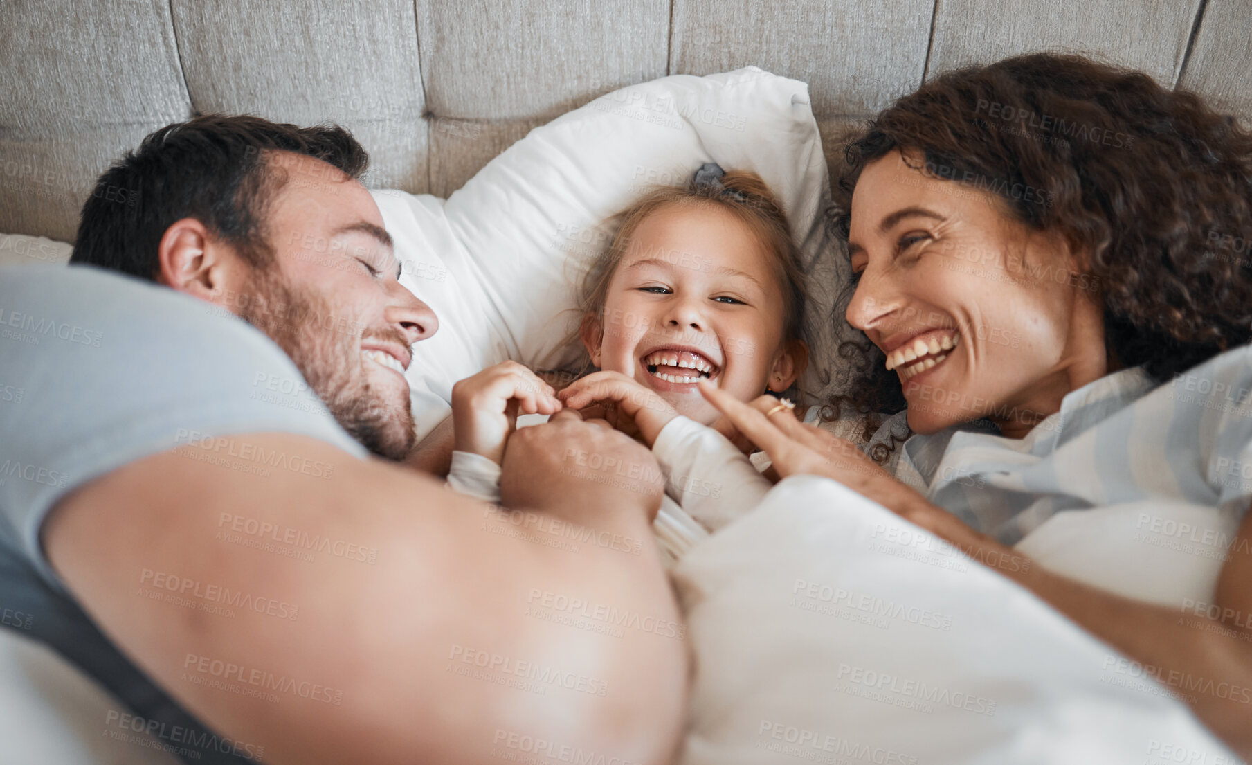 Buy stock photo Family, bedroom and parents laughing with their daughter in the morning to relax after waking up together. Kids, love or smile with a man, woman and cute child having fun in the bed from above