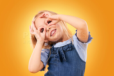 Buy stock photo Kids, fun and hand glasses by girl in studio playing, free and funny gesture against orange background space. Finger, frame and child with silly expression, mood or personality, playful or games