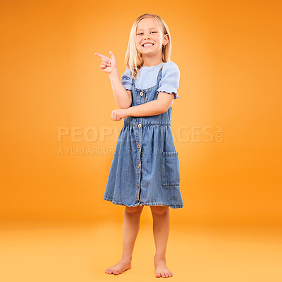 Buy stock photo Pointing, happy portrait and child in studio for advertising, announcement or promotion. Excited barefoot girl kid on a orange background for hand gesture, sale or sign for mockup space or fashion