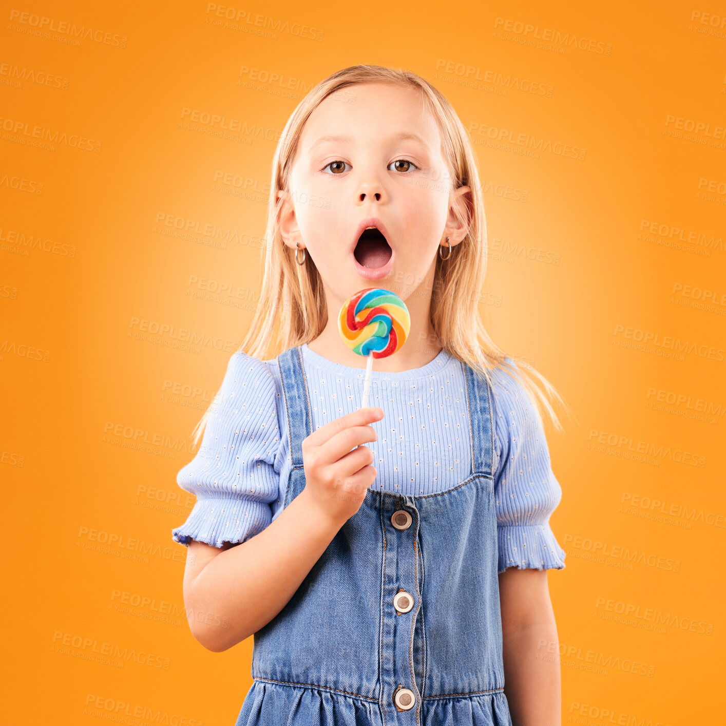 Buy stock photo Candy, girl child and portrait of lollipop in hand, open mouth and studio for sweets, birthday party or carnival. Sugar, kid and eating spiral snack for dessert, hunger or meal on orange background