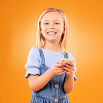 Child, portrait and typing with smartphone in studio for social media, play mobile games and smile on orange background. Happy girl kid, phone and reading notification, watch multimedia and tech app