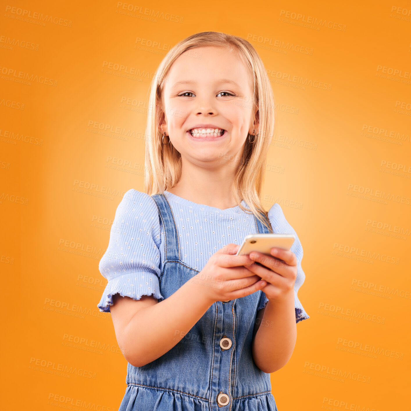 Buy stock photo Child, portrait and typing with smartphone in studio for social media, play mobile games and smile on orange background. Happy girl kid, phone and reading notification, watch multimedia and tech app