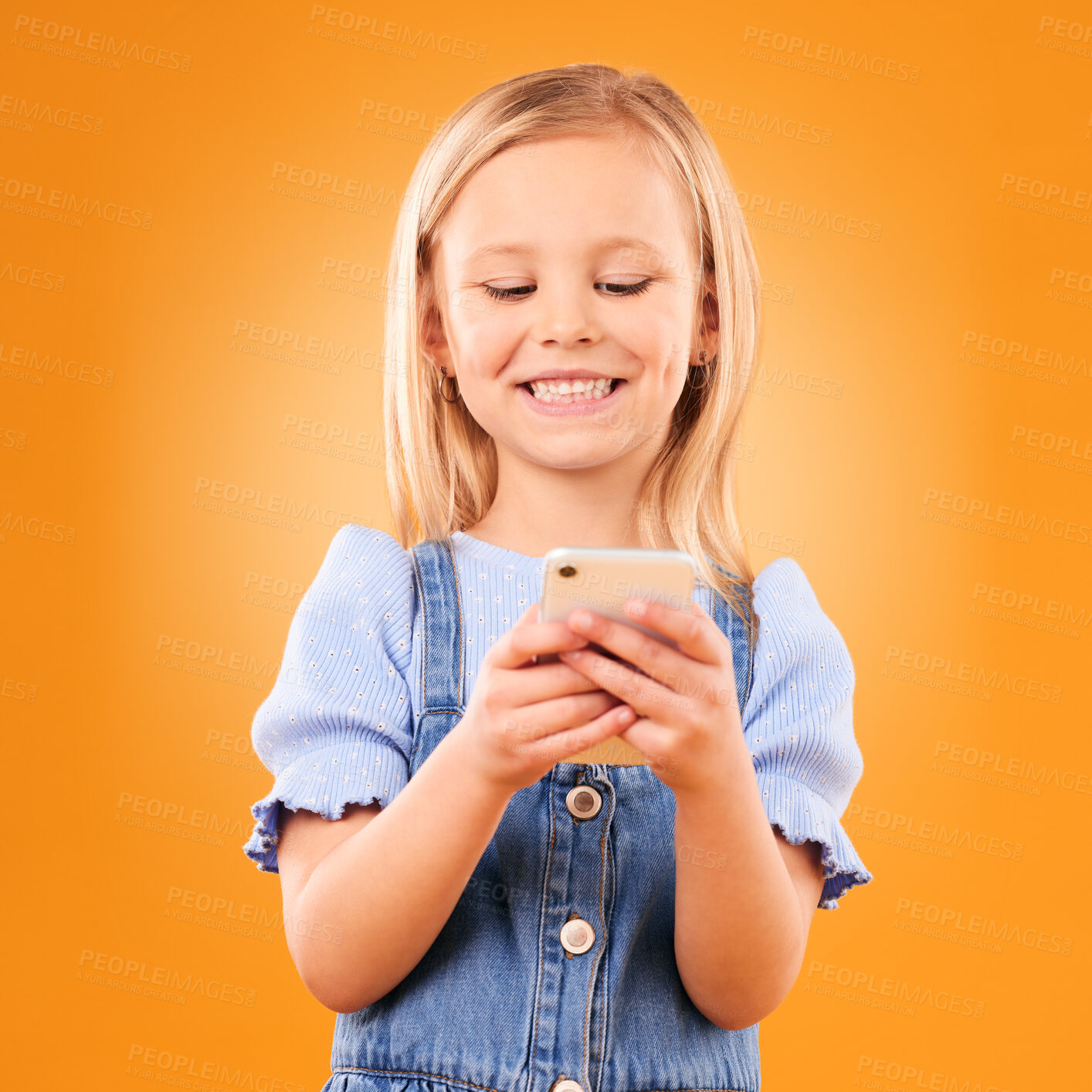 Buy stock photo Child, smile and typing with phone in studio for social media, play mobile games and download app on orange background. Happy girl kid, smartphone and reading notification, watch multimedia and chat