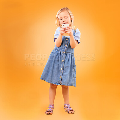 Buy stock photo Girl, child and typing with phone in studio for social media, play mobile games and download app on orange background. Young kid scroll smartphone to search website, watch multimedia and subscription