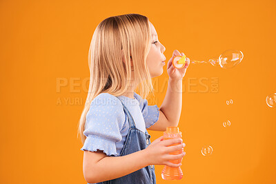 Buy stock photo Girl, child and blowing bubbles in studio for fun, games and childhood development on mockup orange background. Profile of kid playing with soap bubble wand, toys and breathing activity for freedom