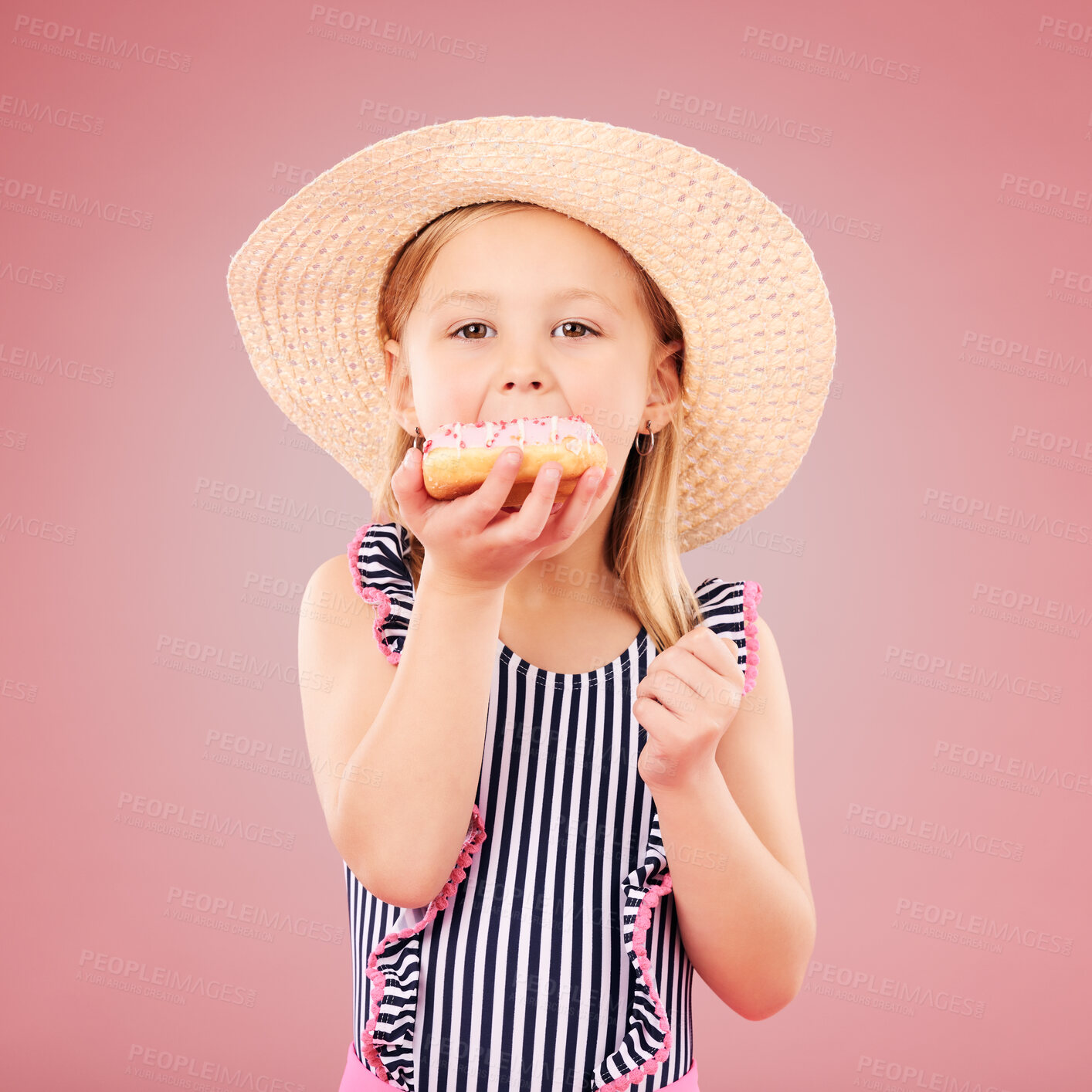 Buy stock photo Girl kid, eating a donut and dessert, sweets and summer with hat and bathing suit isolated on pink background. Portrait, youth and cake with snack, child enjoying bakery treat with hat in studio