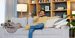 Carefree young man on the sofa to sit and relax at home. Happy guy smiling and laughing while watching funny videos, series or movies on the TV in his living room over the weekend