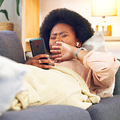 Bored and tired woman lying on a couch typing on her phone at home. A ...
