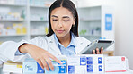 A young female pharmacist stocktaking in a dispensary using a tablet. Doctor preparing prescriptions and medication at clinic or pharmacy. Healthcare professional sorting medicine with digital device