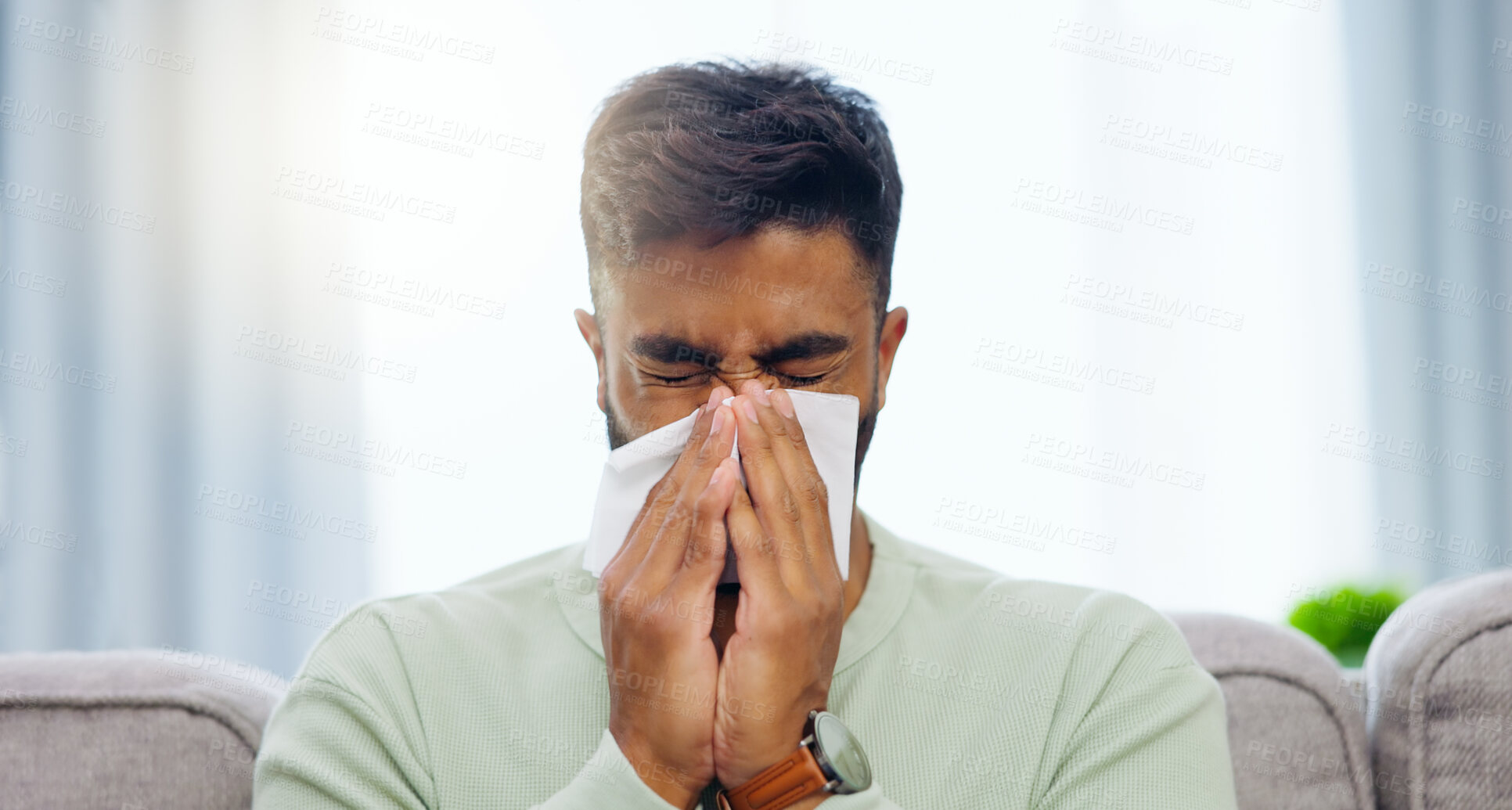 Buy stock photo Tissue, sneeze and Indian man blowing nose on a home living room sofa feeling sick and tired. Allergy problem, virus and toilet paper of a person on a house lounge couch with sinus infection and flu