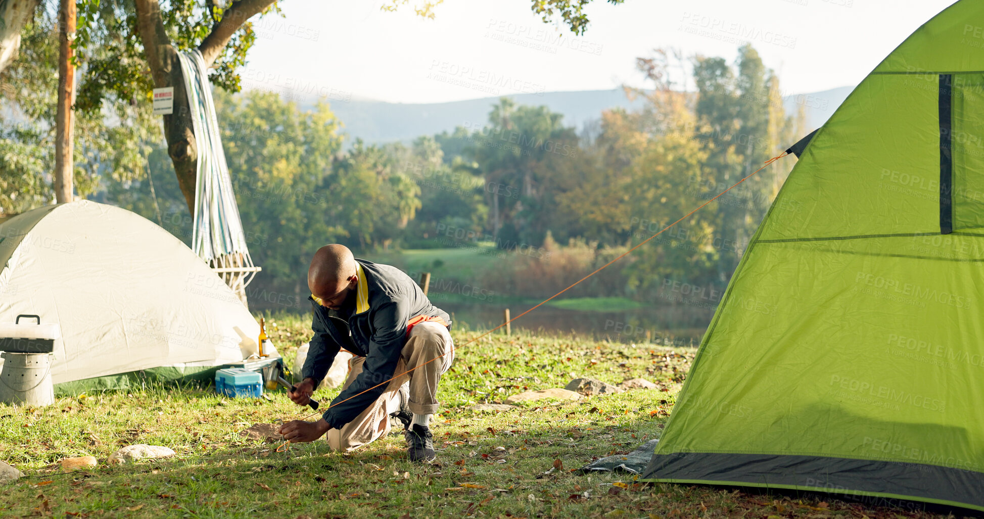 Buy stock photo Camping, tent and black man setup in woods for shelter on outdoor holiday, vacation and adventure, Campsite, traveling and male person with hammer for pins for gear in nature, forest and countryside