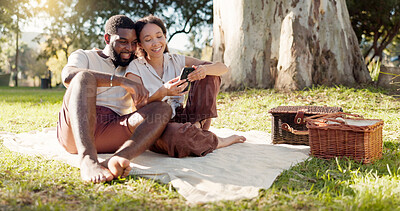 Happy, social media and an interracial couple on a picnic with a phone for communication, tech or an app. Talking, summer and a black man and woman with a mobile for a chat on a date in a park