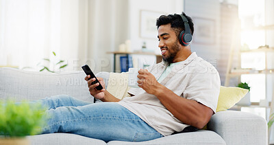 Coffee, phone and happy man on sofa with headphones for social media, video streaming service and networking mobile app. Indian person relaxing on couch in his apartment on audio tech and smartphone