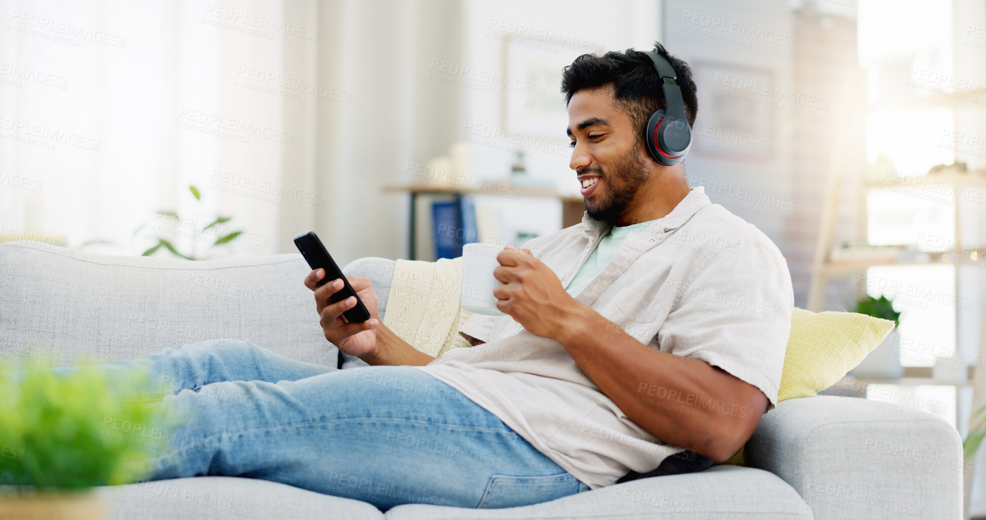 Buy stock photo Coffee, phone and happy man on sofa with headphones for social media, video streaming service and networking mobile app. Indian person relaxing on couch in his apartment on audio tech and smartphone