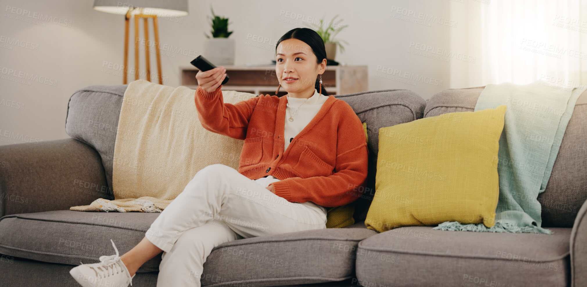 Buy stock photo Watching tv, relax and an Asian woman on a sofa in the living room of her home streaming a subscription service. Television, channel surfing and comedy with an attractive young female sitting in her lounge