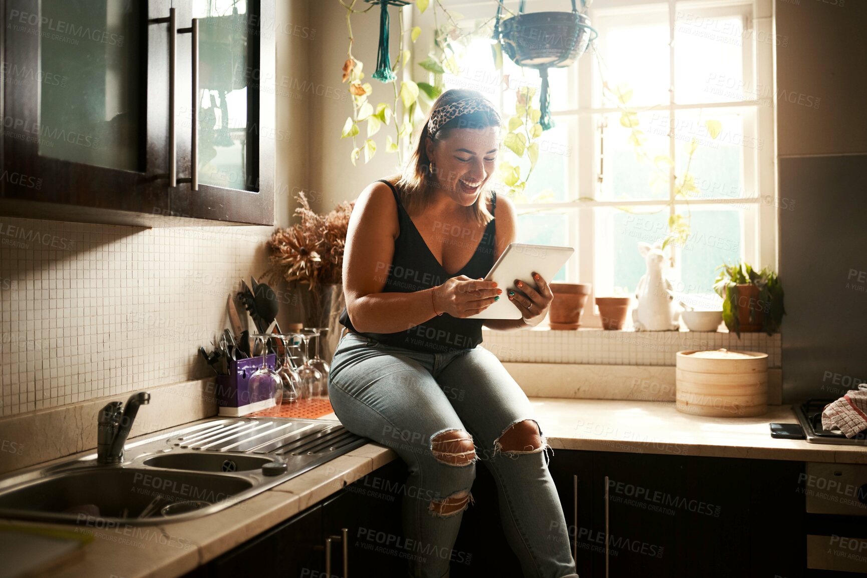 Buy stock photo Browsing social media on tablet, searching online and reading funny stories, gossip and articles on technology app in home kitchen. Smiling and happy woman sitting on countertop and playing games