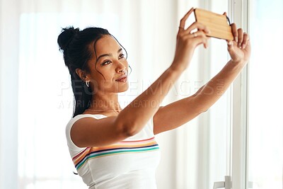 Buy stock photo Cropped shot of an attractive young blogger standing in her home and using her cellphone to take a selfie