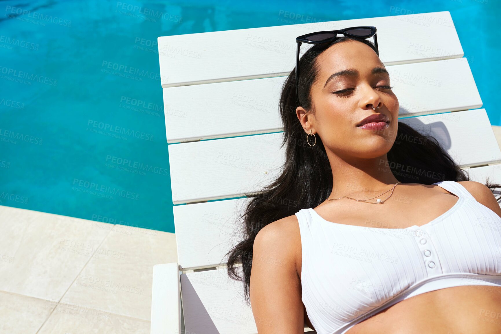 Buy stock photo Cropped shot of a beautiful young woman relaxing on a lounger by the poolside