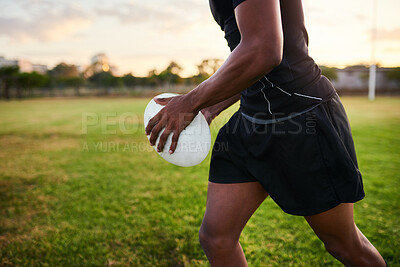 Buy stock photo Cropped shot of an unrecognizable sportsman standing alone and holding a rugby ball before an early morning practice
