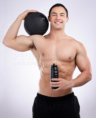 Buy stock photo Shot of a male athlete holding a medicine ball and water bottle against a studio background