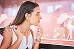 Young woman looking at jewellery on display through a window during a shopping spree in a mall. One female only doing window shopping. Shopaholic holding bags and deciding whether to buy accessories