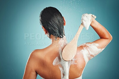 Buy stock photo Skincare, back and woman in a shower for cleaning, hair and wellness against a blue background mockup. Beauty, brush and skin, scrub and exfoliate by girl model in a studio, relax and washing  