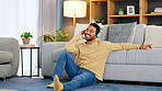 Happy relaxed man listening to music using headphones while sitting on the floor of his house. Young male relaxing at home enjoying his comfort and favorite song. A carefree guy having fun