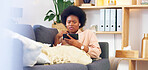 Sick and tired woman lying on a couch typing on her phone at home. A young African female relaxing and yawing on a sofa in her house on a boring weekend. A sleepy lady scrolling social media