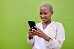 Black woman, typing and phone for communication by a wall or green background with internet. African person with a smartphone reading social media message, networking and mobile app chat space