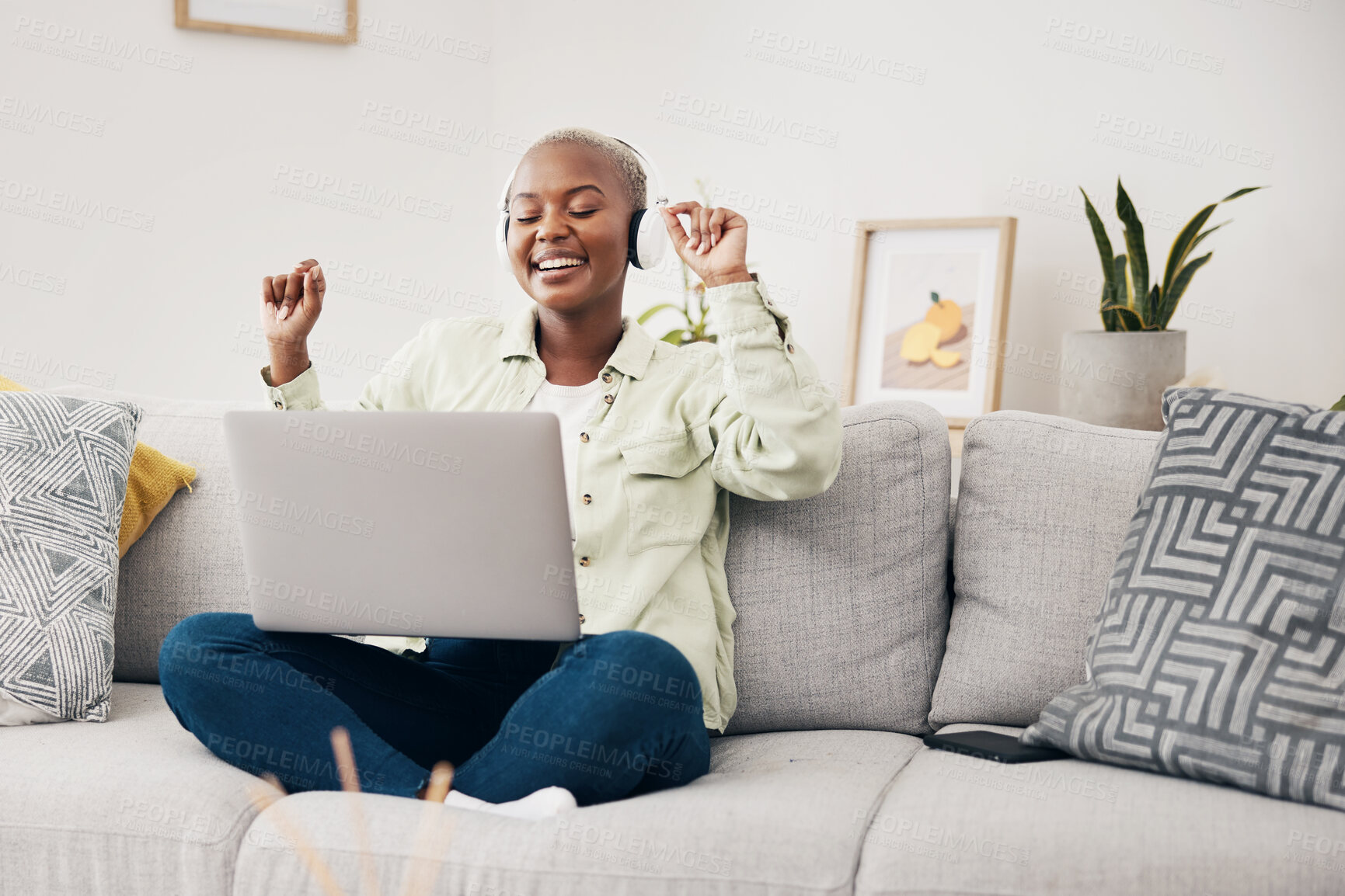 Buy stock photo Laptop, music and black woman dance on a sofa with headphones, free and happy in her home. Podcast, earphones and African female dancing to feel good radio, audio or album playlist in a living room