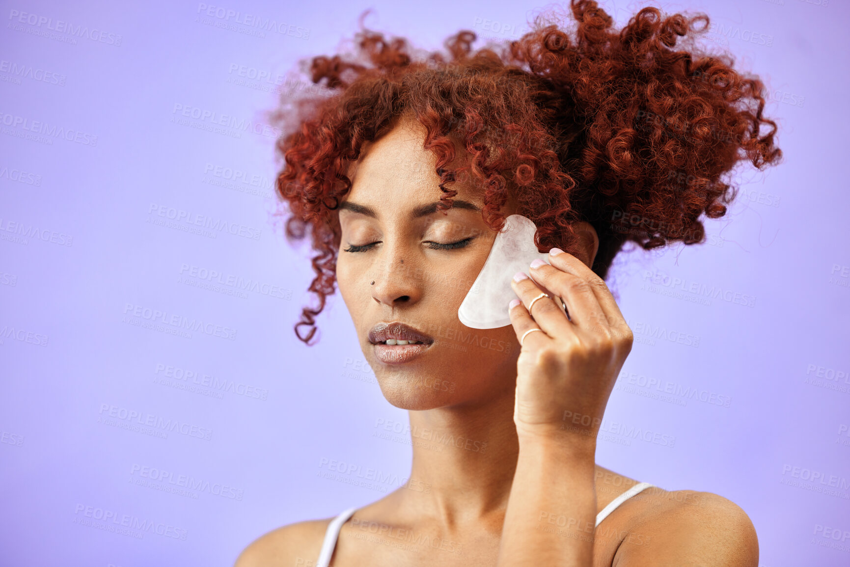 Buy stock photo Skin, gua sha and skincare, woman and beauty with cosmetic tools isolated on purple background. Red hair, curls and facial massage with stone, dermatology and wellness with face glow in a studio