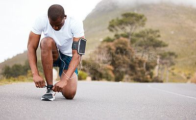 Fitness, tie or runner with shoes on a road by nature for exercise, training or outdoor workout. Sports race, black man or healthy athlete on street with footwear or headphones for streaming music