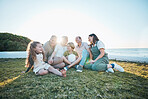 Family, grandparents and children on grass by ocean for bonding, relationship and relax together. Nature, parents and happy grandmother, grandfather and kids on holiday, vacation and travel by sea