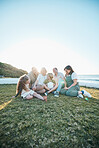 Family, grandparents and kids on grass by ocean for bonding, relationship and relax together. Nature, parents and happy grandmother, grandfather and children on holiday, vacation and travel by sea