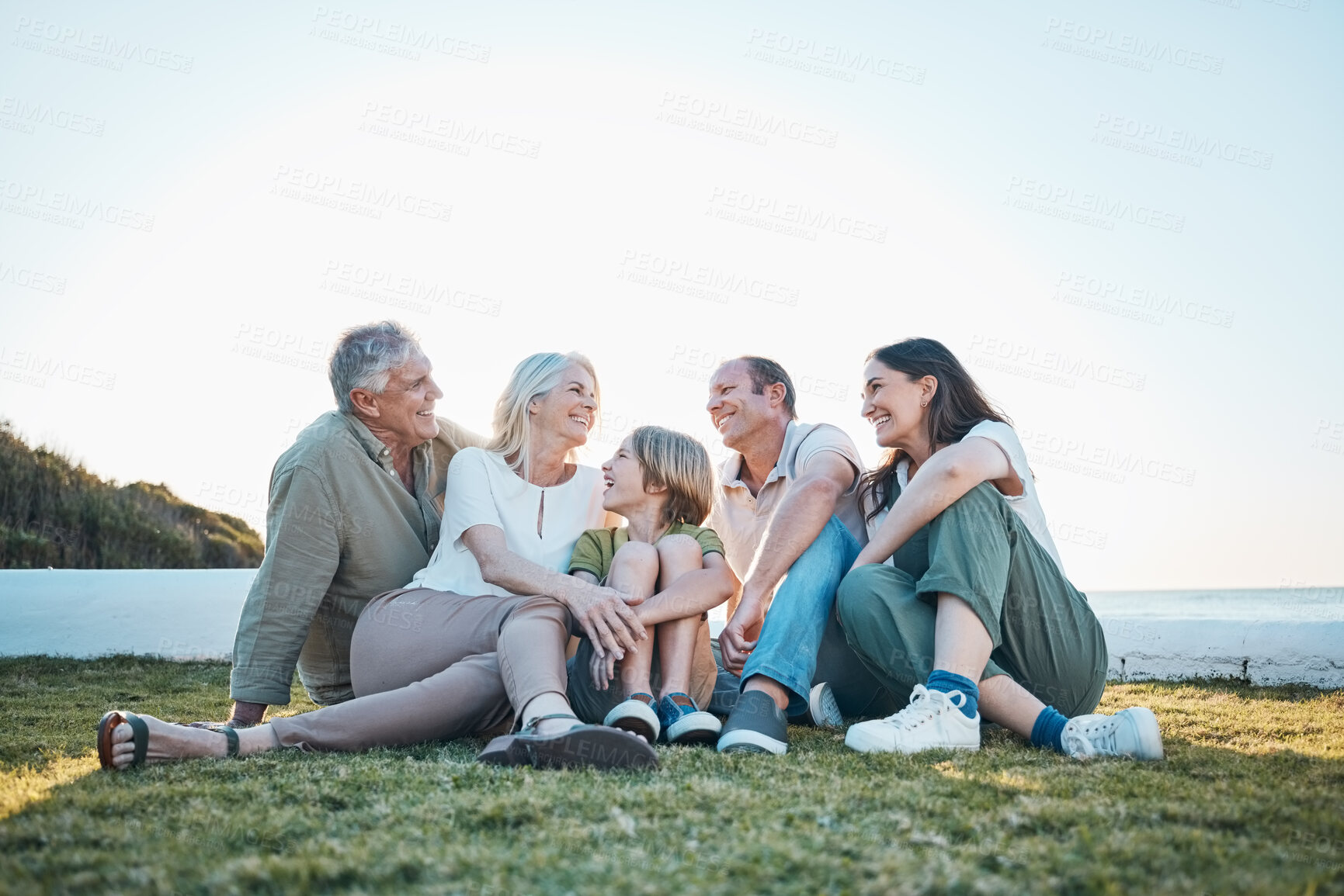 Buy stock photo Parents, grandparents and a child outdoor on grass with a smile, love and care in summer. Men, women and kid or happy family at park in nature for holiday, vacation and travel by sea with sky banner