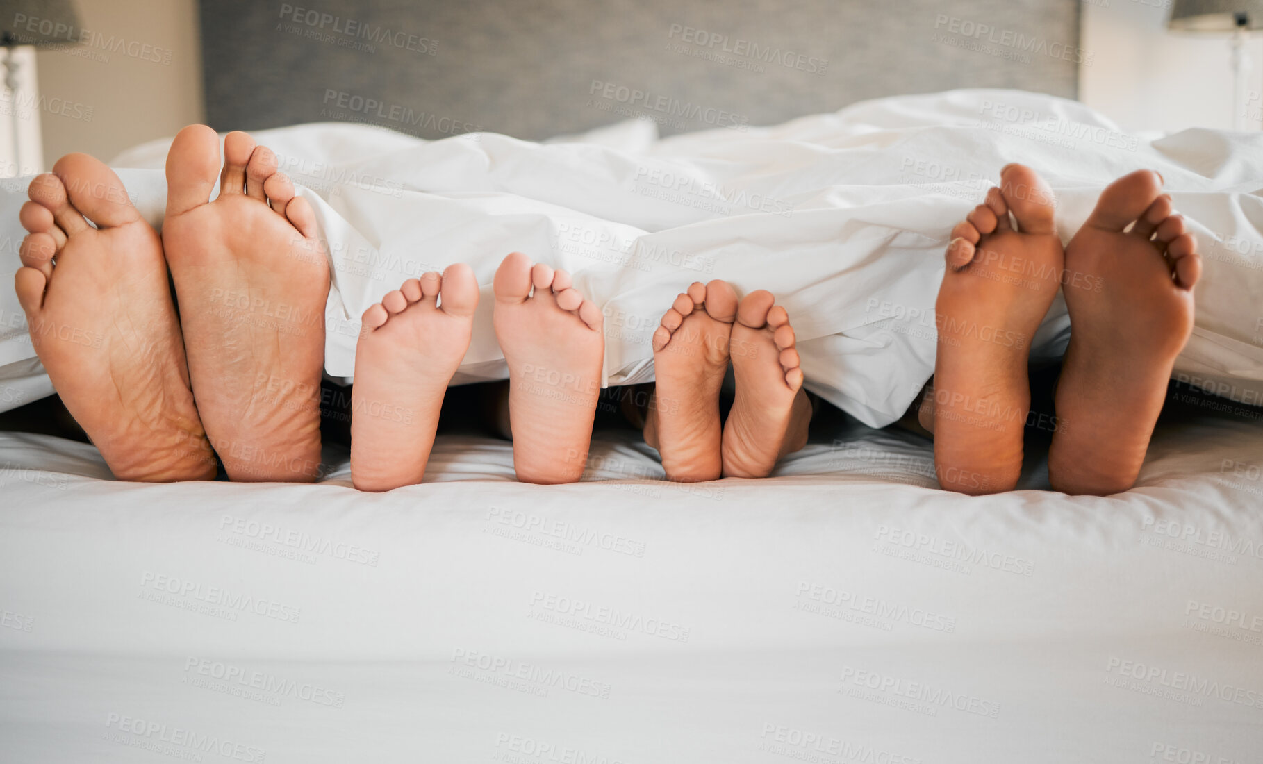 Buy stock photo Feet, bed and family relaxing at their home for bonding, sleep and resting together on a weekend. Love, calm and closeup of parents laying with children in bedroom in the morning at modern house.