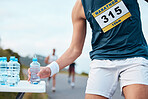 Hand, water and running a marathon race for competition closeup with fitness or cardio on a street. Sports, exercise or health with  runner or athlete grabbing a drink while on a road for training