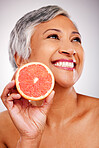 Senior, happy woman and face with grapefruit for vitamin C, skincare or natural nutrition against a studio background. Mature female person smile with organic citrus fruit for collagen, detox or diet