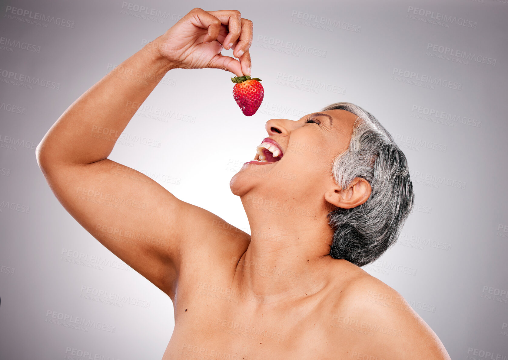 Buy stock photo Beauty, health and mature woman with strawberry in a studio eating a diet snack for wellness. Skincare, cosmetic and female model with a fruit for anti aging, nutrition treatment by gray background