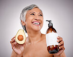 Senior woman, avocado and studio with smile for bottle, product and ideas for nutrition by white background. Mature female model, fruit and thinking for cleaning, beauty or skincare with organic oil