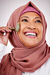 Muslim woman, facial roller and skin care in studio with quartz for dermatology, cosmetics and glow. Happy mature female person with islam hijab, face massage and beauty on a white background