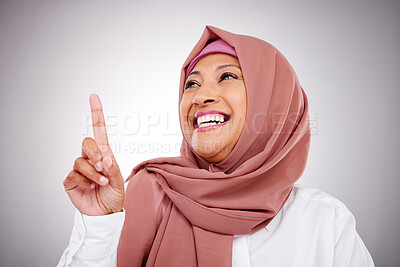 Buy stock photo Pointing up, happy and face of Muslim woman in studio with makeup, cosmetics and beauty. Fashion, style and and Islamic person with hand gesture for news, promotion and show on gray background