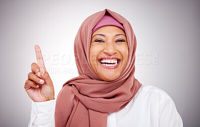 Buy stock photo Pointing up, happy and portrait of Muslim woman in studio with makeup, cosmetics and beauty. Fashion, style and face of Islamic person with hand gesture for promotion, news or show on gray background