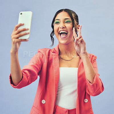 Buy stock photo Phone, selfie and woman with a peace sign from social media and profile picture for creative job in studio. Influencer, happy and makeup with career fashion with blue background and emoji hand sign