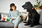 Woman, reading a book and a dog on home sofa to relax with animal in a living room. Pet owner, happiness and a young person on a couch with love, care and wellness or friendship in a cozy apartment