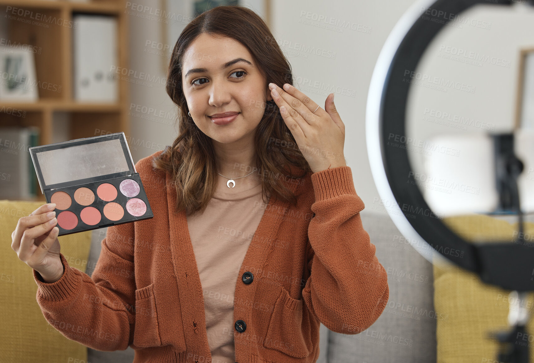 Buy stock photo Streaming, makeup and review with a woman influencer in her home to broadcast live content to viewers. Social media, product or tutorial with a young brand ambassador in the living room for cosmetics