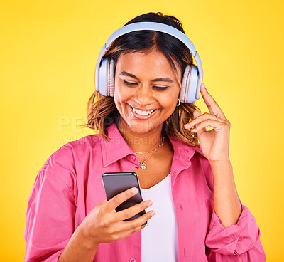 Buy stock photo Headphones, phone and young woman in a studio listening to music, playlist or radio and networking. Happy, cellphone and female model from Mexico streaming a song or album by yellow background.