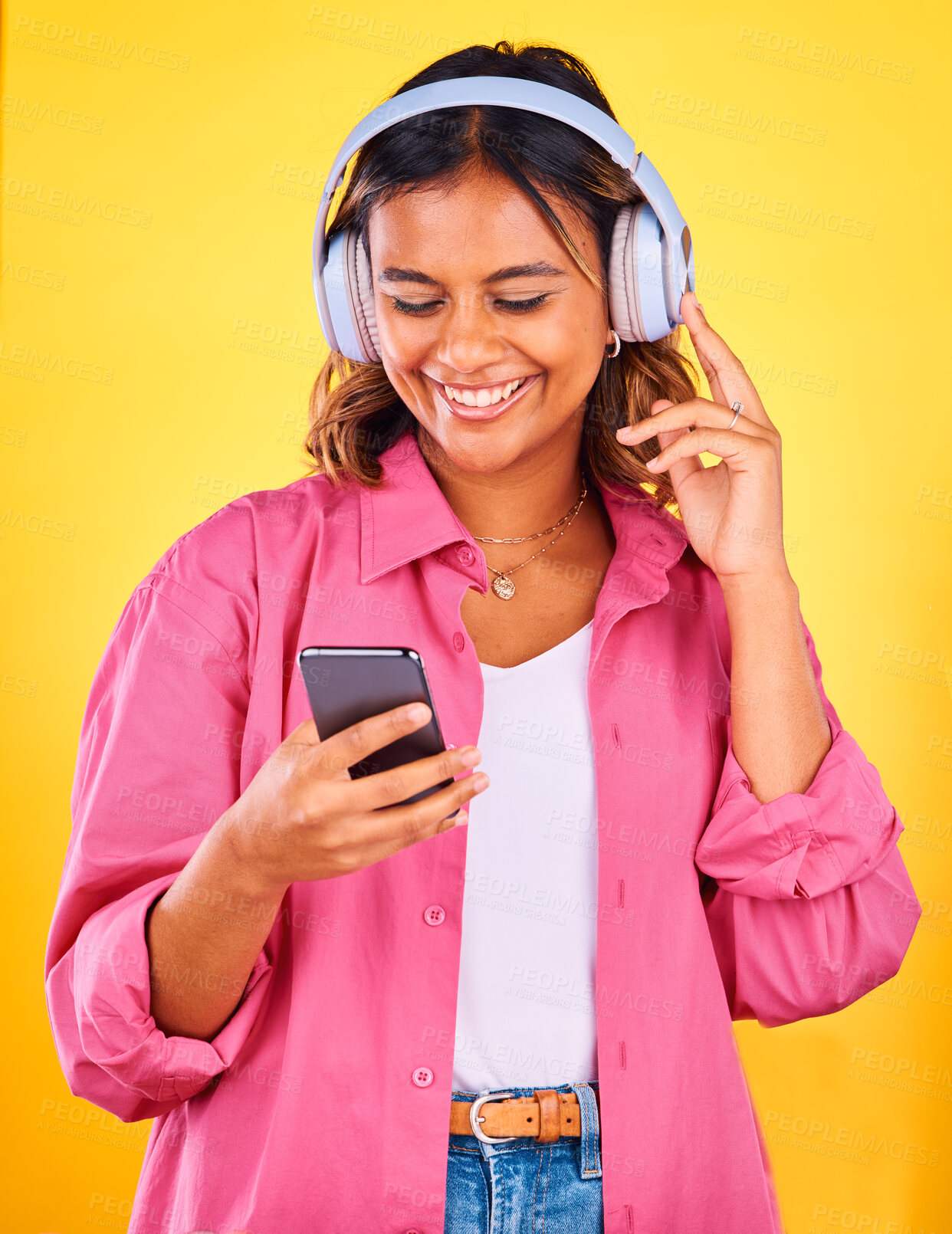 Buy stock photo Headphones, cellphone and young woman in a studio listening to music, playlist or radio and networking. Happy, phone and female model from Mexico streaming a song or album by yellow background.